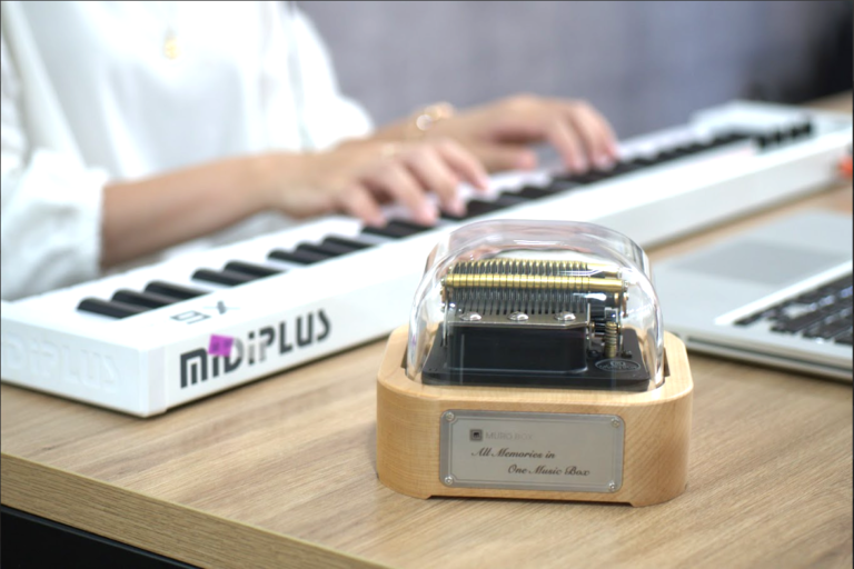 前にあるのはスマートオルゴールMuro Box-N20標準版で、アレンジャーがMIDIキーボードでオルゴールをコントロールし、自分が弾いているメロディーをオルゴールに演奏させ、お客様のカスタマイズ編曲の演奏エフェクトを試聴しています。