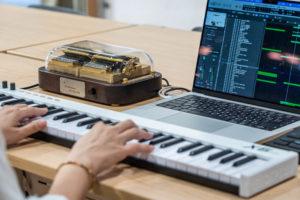 The music arranger is using a MIDI keyboard and a laptop to arrange melodies for playing on the Muro Box-N40 Sublime music box.