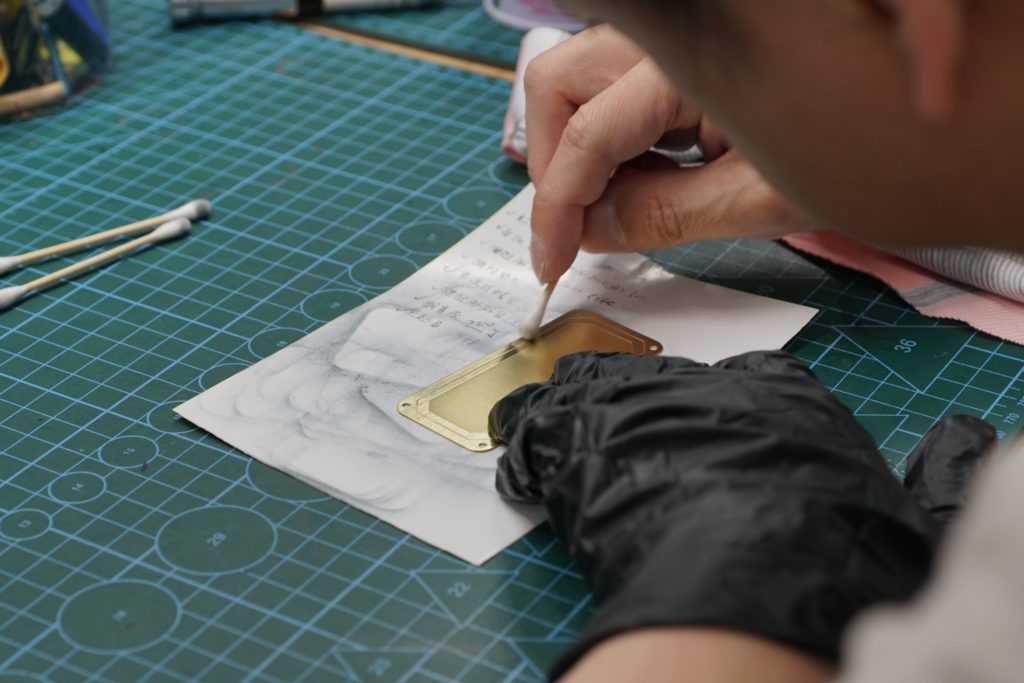 The process engineer is currently applying rust prevention treatment to the brass nameplate of the music box, applying rust-proof oil and wiping it clean.