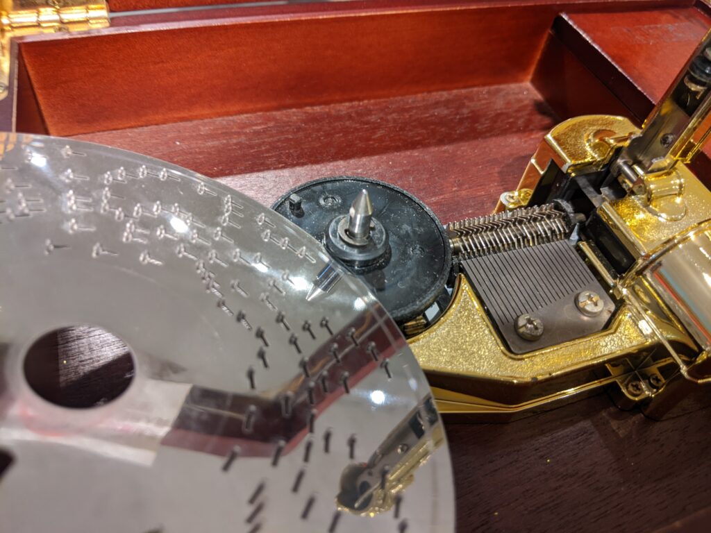 23音階金屬唱盤式音樂盒背面展示，含金屬凸點圓盤、星形爪盤與馬達蓋。