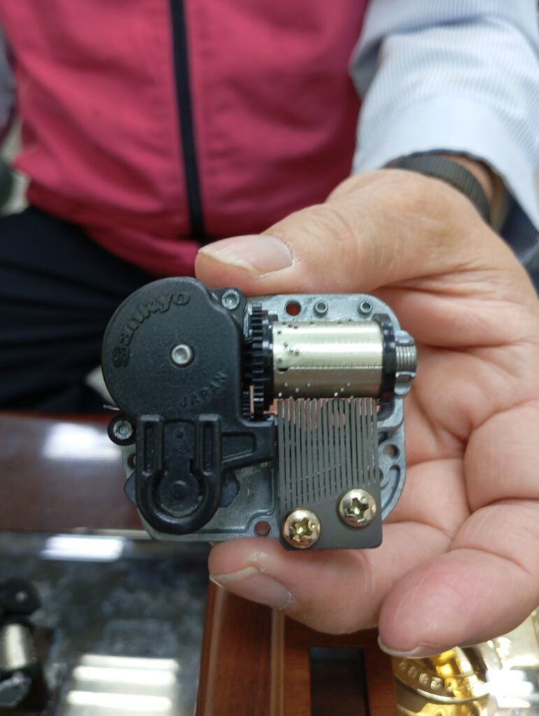 黃總經理展示早期日本製的 Sankyo「3S」音樂鈴機芯，特徵為黑色發條盒蓋與「JAPAN」字樣。