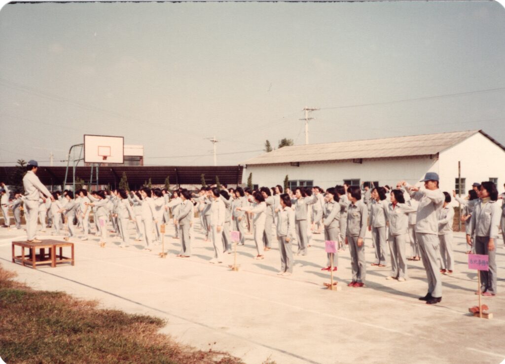 早上十點一到，廣播響起體操音樂，員工原地起立做晨操。照片中應是團康活動，大家集中在操場一起體操。