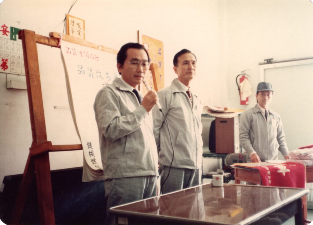 品質月間成果發表會議。持麥克風者為第二任總經理大久保學，中間為總務課長吳雙盈，主席台站立者為製造部經理黃龍溪。
