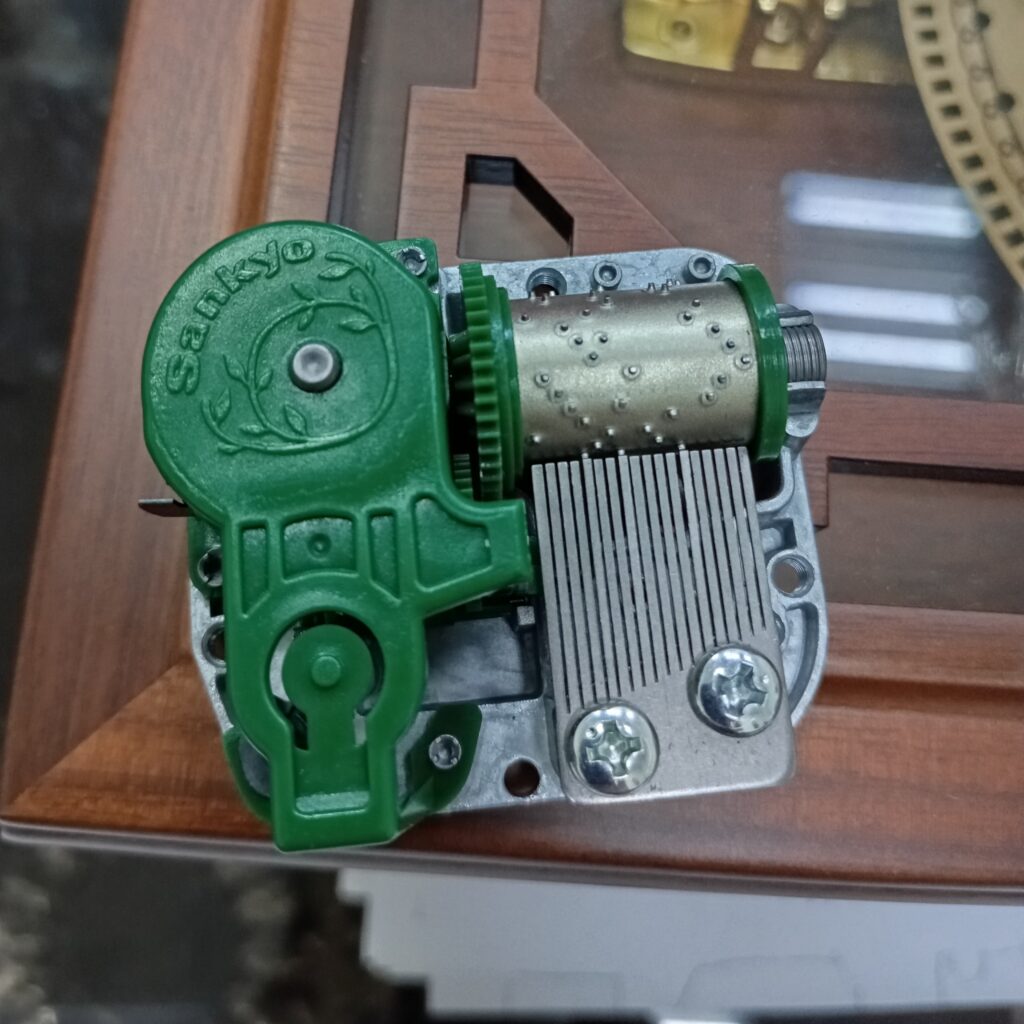 綠色 5S 音樂鈴機芯，止速閥支架固定於蓋面與鋅合金基座，提升運輸耐性。