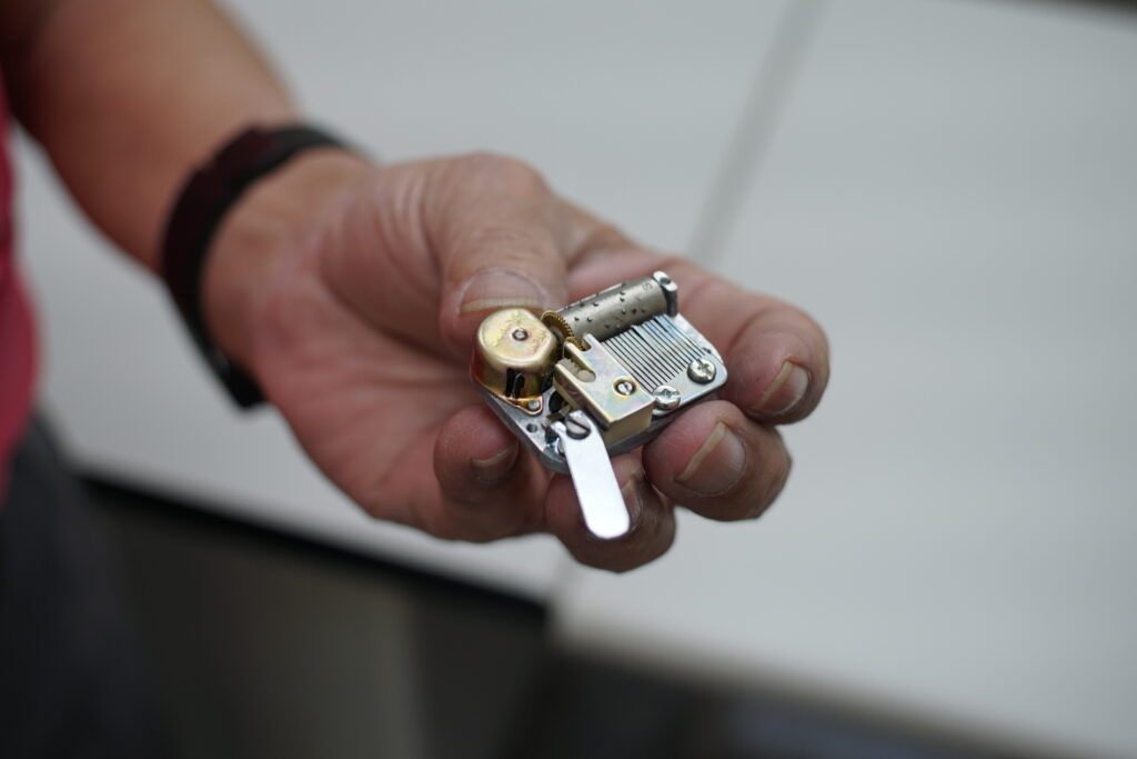 手中的迷你音樂鈴機芯，是最初由日本 Sankyo 設計的版本，特徵是大部分零件仍為金屬製造。