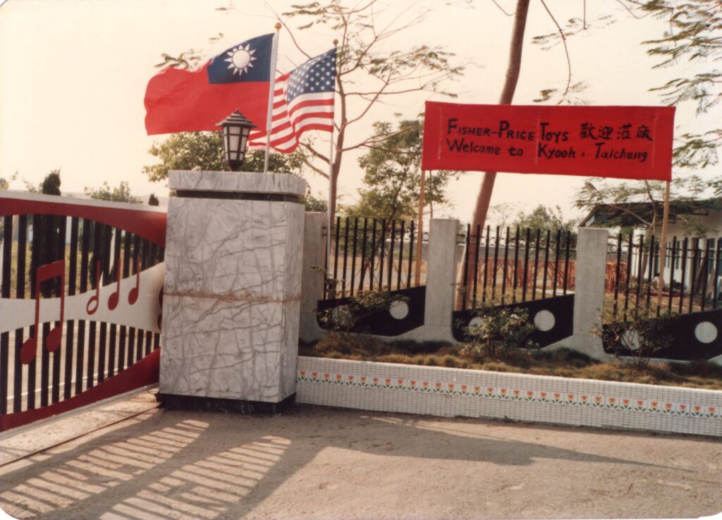照片中插著台美兩國國旗，門口布條寫著「Fisher-Price Toys 歡迎蒞廠」「歡迎到協櫻，台中」。協櫻早期曾與美國知名兒童玩具品牌 Fisher-Price 有合作關係。