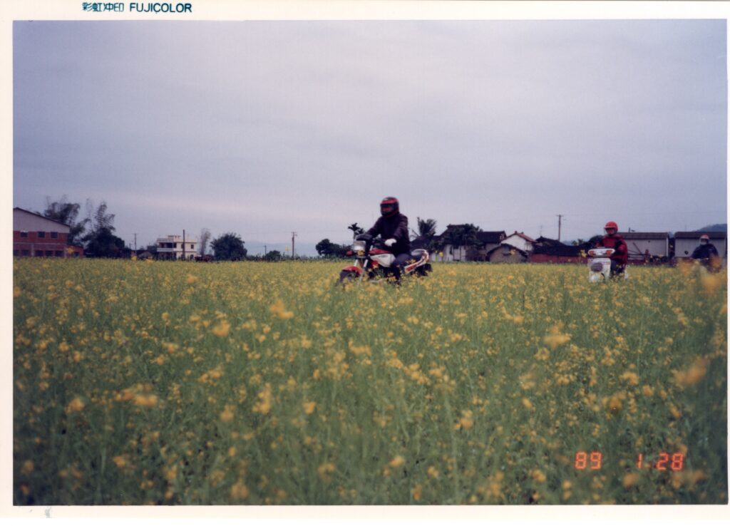 近四十年前騎車在霧峰的油菜花田小徑裡。令人驚訝的是，霧峰的風景至今幾乎沒有改變。途中機車疑似光陽王牌HS135，歡迎提供正確車型資訊。