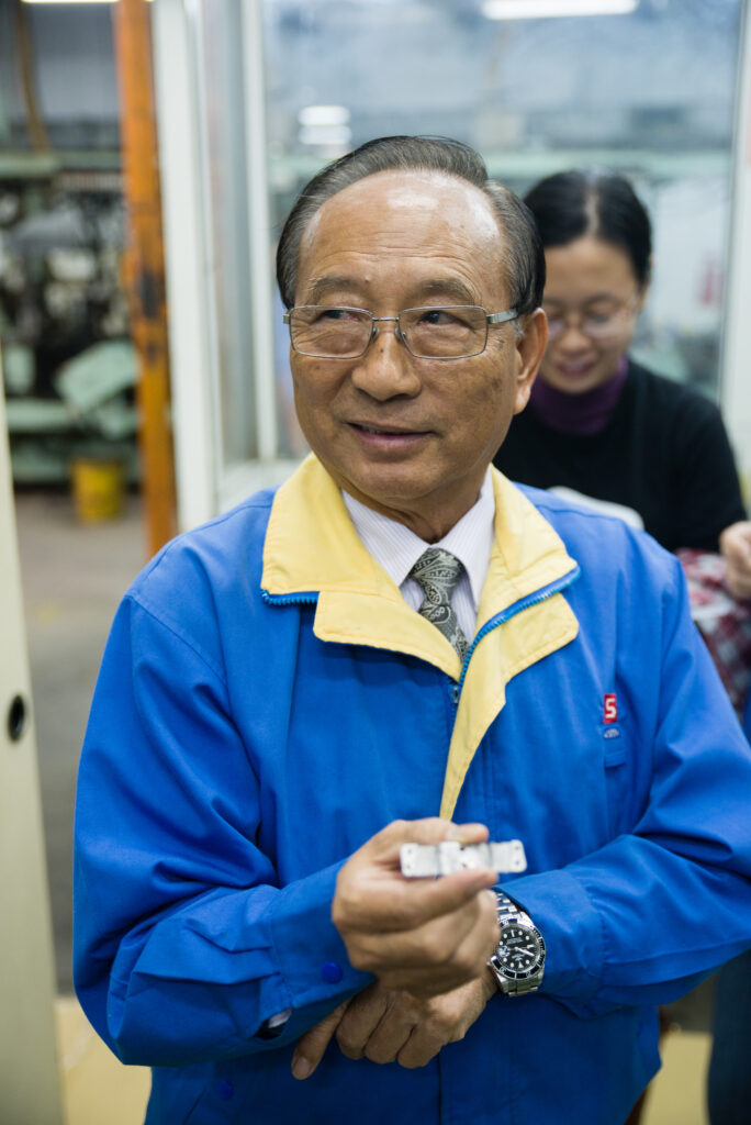 黃總經理手持迷你機芯震動板半完成品。當公司面臨虧損，他挺身而出，展現台灣人拚搏精神。